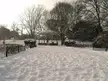 A white gazebo in a snowy park with bare trees and two people in dark clothing.