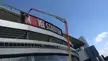 A worker in orange clothing using a cherry picker lift to install a 'MARVEL STADIUM' sign on a stadium building.