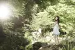 Yuna Kim in a light blue mini sundress standing on a rock in a sunlit forest