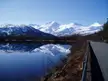 E6 south of Narvik featuring snow-capped mountains reflecting in a calm lake beside a paved road with a guardrail.
