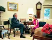George W. Bush in a dark suit and red tie talking with Trude B. Feldman in a pink dress and black boots.