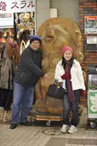 A smiling couple with tanned skin posing next to a large wooden bear carving in Sapporo.