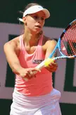 Magda Linette in a pink tank top and white visor hitting a tennis ball on a court