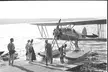 Waco RNF LN-EAB seaplane docked at a pier with a group of people in swimwear and bikinis