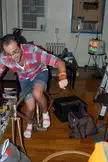 Dave in a plaid shirt and denim shorts stepping over a bicycle frame in a room