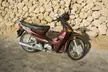 Maroon Honda Wave motorcycle parked against a light-colored stone wall