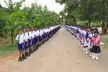 Students in white shirts and blue skirts at Mahadeva Achchirama Children Home standing in lineups on a dirt road