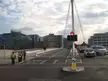 Bus lane on a city street with a bridge, cable mast, and people walking, including one in a neon yellow safety vest.