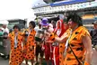 A group of people dressed as The Flintstones in orange leopard print costumes and shaggy wigs near a stadium grandstand.