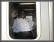 Duane, a smiling plus-size man in a white short-sleeved uniform shirt, waves from an AMTRAK Capital Limited vehicle doorway.