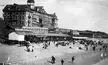 Santa Monica State Beach with the Arcadia Bath House, a large hotel, and people in vintage white dresses and suits.
