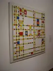 Abstract oil painting with a grid of red, yellow, and blue squares on a white wall in an art gallery.