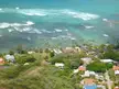 Aerial view of a tropical coastal neighborhood with houses, palm trees, and turquoise ocean waves