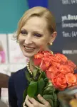 Russian ballet dancer with blonde hair in a bun smiling and holding orange roses