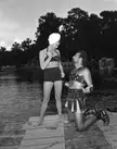 Esther Williams in a bikini and headwrap holding a sword over Howard Keel in Roman costume on a wooden dock