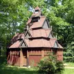 Saint Swithuns Church, a replica stave church with a multi-tiered wooden roof surrounded by green trees and grass