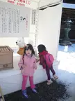 Two Japanese girls in winter clothes standing by a white booth with a dog statue in the snow at Kotohira-gu