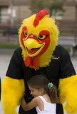 A person in a yellow chicken mascot costume hugging a girl in a white dress.