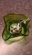 Close-up looking down at a luxury silver watch with a metal link band inside a wavy green glass bowl