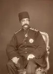 Tabriz vintage photo of a man in a dark military uniform with medals and a tall hat seated in an ornate chair