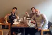 Gurba, Bowles, and Lovato sitting around a wooden table with coffee and plates in a casual indoor setting.