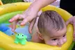 Baby with wet hair and funny faces in a yellow inflatable pool with a green frog toy