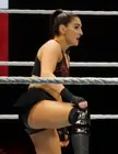 Deville in black athletic wear, including a tank top and short skirt, posing in a wrestling ring