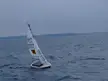 ASV Roboat sailboat with a white sail navigating choppy blue ocean waters under a cloudy grey sky