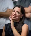 Elena Manferdini smiling, wearing a black sleeveless satin dress with long dark hair and red nail polish