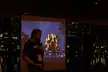 Man with a tattoo sleeve and glasses standing before a colorful light installation projection
