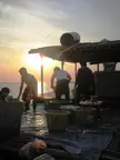 A group of people in casual white shirts and trousers working with baskets on a boat deck at sunset