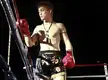 Tetsuya Yamato in a boxing ring wearing red boxing gloves, black shorts, and a headband