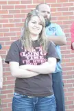 Blonde woman in a brown t-shirt and skinny blue denim jeans standing with a man against a brick wall