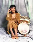 Geneviève McKenzie-Sioui with dark hair and pale skin wearing a brown costume and beaded necklace among drums