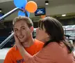 A woman with long brown hair in a peach shirt kissing a man in an orange t-shirt on the cheek.