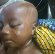 Close-up of a bald baby with dark skin and tribal marks on their face and head.