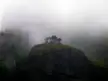 Meteora landscape photography featuring a small cluster of trees atop a dark rocky peak in thick fog and misty mountains