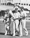 Don Bradman in white cricket gear being carried on the shoulders of opponents across a field