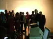 A group of 13 people at a final show_LCC, including women in red, blue, and floral dresses and a man by a projector.