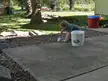 Blonde girl in a grey t-shirt using a small shovel on a concrete patio next to a white bucket