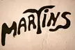The word 'MARTINS' in a stylized black hand-drawn font on a textured light-colored wall