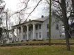 The Mansion house, a weathered white house with columns on a grassy hill behind a stone wall