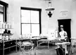 A nurse in a vintage uniform and cap standing in the Pemberton Memorial operating room with surgical equipment.