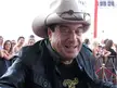 Smiling man in a beige cowboy hat and black leather jacket with a group of people behind him