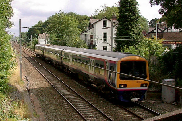 A train passing through Cheadle Hulme towards Handforth. The white building in the background is the original station house.