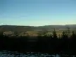 Fischbach Alps landscape with rolling green hills, forests, and snow-capped mountains under a blue sky