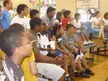 A group of friends in athletic wear and white shirts sitting on benches in a San Antonio gym with balloons and a banner