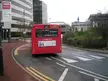 The 369 red Stagecoach bus driving away on an urban city street past a modern office building