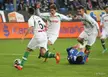 Vranješ and other soccer players in white and blue athletic wear competing for a ball on a green field