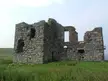 Ruins of Whitefield Castle, a stone building in a grassy field under a pale sky